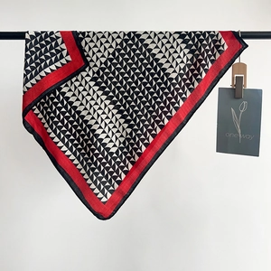 Dettaglio di un foulard in seta rosso e nero con motivi a lettera H e trame geometriche