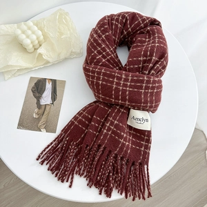 Cozy burgundy plaid winter scarf with tassels and brand label on a white tabletop