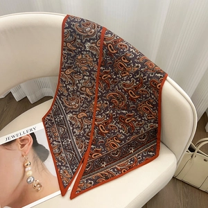 Détail d'un foulard en soie à motif paisley marron et orange posé sur une chaise