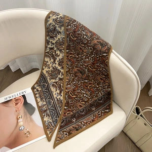Détail d'un foulard en soie à motif paisley marron et doré drapé sur une chaise chic
