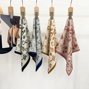 Detail showing four silk square scarves with floral and heart prints on wooden hangers