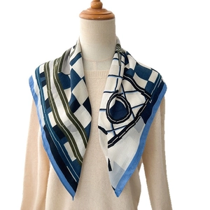 Modern geometric silk scarf with blue and white pattern on a mannequin with beige knitwear