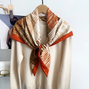 Detail of silk-feel geometric print scarf in orange and brown paired with a beige knit sweater