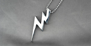 Detailed close-up of a silver lightning bolt pendant on a textured grey fabric background