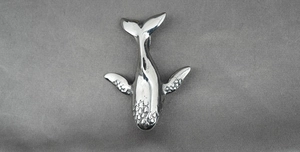 Détail macro du pendentif baleine en métal argenté avec textures réalistes et queue polie