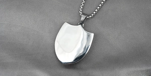 Detailed close-up of shield-shaped stainless steel pendant with high-polish mirror finish