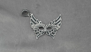 Macro shot of silver winged mask pendant with black zircon inlays and feather texture
