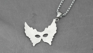 Close-up of silver winged mask pendant on a box chain with detailed metal texture