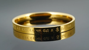 Macro view of gold stainless steel bangle featuring engraved Buddhist mantra with reflection