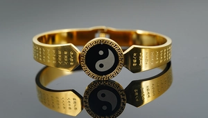 Macro shot of gold-plated titanium steel bracelet featuring Tai Chi symbols and sutra engraving