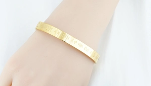 Detailed close-up of gold titanium steel bangle with engraved Buddhist mantras for women