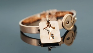 Macro detail of rose gold heart lock bangle and key pendant with brushed metal finish