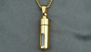 Close-up of golden cylinder pendant necklace with transparent window on grey fabric
