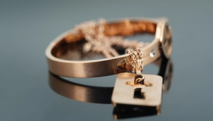 Close-up of rose gold bangle with key pendant and arrow relief detail on dark surface