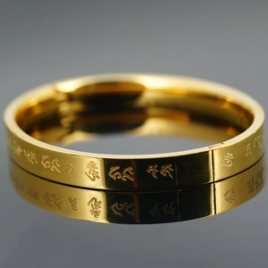 Polished gold stainless steel bangle with engraved Buddhist mantras on a reflective surface