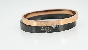 Détail de bracelets de couple or rose et noir avec texte gravé et incrustation croix