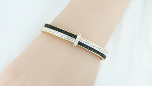 Macro detail of gold-plated open bangle featuring black and white pave-set stones