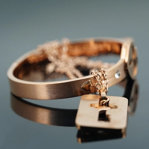 Rose gold titanium bangle featuring arrow clasp with square lock pendant and white crystal