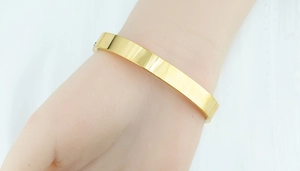 Detailed view of polished gold plated titanium steel bangle worn on woman's wrist