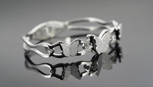 Macro shot of a silver butterfly cuff bracelet with crystals on a dark mirror background