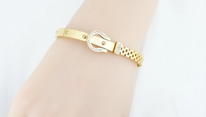 Detail eines goldenen Titanarmbands mit diamantierten Hufeisen-Schnallen und Schraubenmotiv