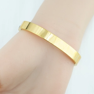 Minimalist flat open cuff bangle in polished gold finish shown on a female wrist