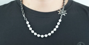 Detail of nautical rudder pendant on asymmetric pearl and metal cuban chain necklace