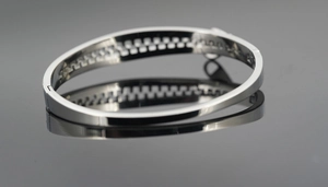 Detail view of silver stainless steel bangle with engraved geometric pattern on the inner ring