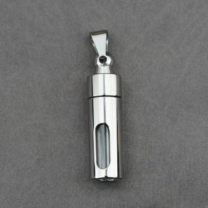 Polished silver cylinder memorial urn pendant with glass window on a grey fabric background