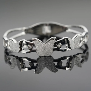 Polished silver butterfly bangle with zirconia stones and woven texture on grey reflection