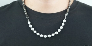 Dettaglio di una collana mista con maglie metalliche e perle bianche su un modello reale