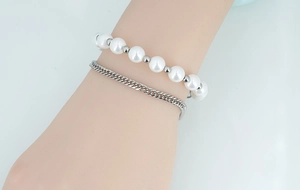 Détail d'un bracelet double couche avec perles blanches et chaîne à maillons argentés au poignet