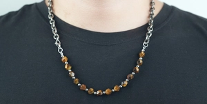 Dettaglio della collana con perle occhio di tigre e catena cubana in acciaio sul modello