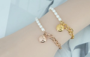 Détail de bracelets superposés en acier titane avec breloque smiley et perles au poignet