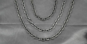 Close-up of three layered vintage black stainless steel Cuban necklaces on gray silk