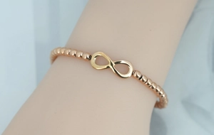 Close-up of rose gold infinity symbol beaded bracelet on wrist showing natural metal luster