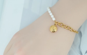 Détail du bracelet en perles et chaîne à maillons dorés avec pendentif visage souriant