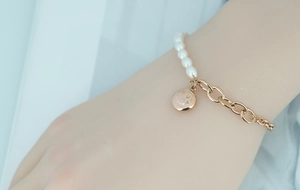 Détail d'un pendentif sourire or rose sur un bracelet asymétrique perles et chaîne