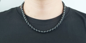 Détail d'un collier en obsidienne avec perles argentées porté par un homme en t-shirt noir