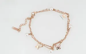 Détail de la chaîne double couche en or rose avec perles synthétiques et papillons