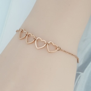 Minimalist rose gold stainless steel bracelet with four hollow heart shapes on model wrist