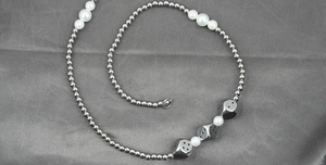 Detail view of pearl and steel bead necklace with square dice charms on grey silk