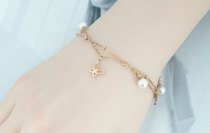 Détail du bracelet double couche en or rose avec pendentif papillon et perles blanches