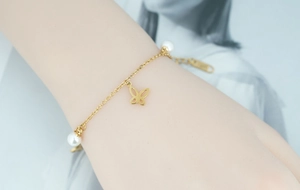 Détail d'un bracelet en acier titane doré orné de breloques papillon et perles blanches