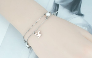 Détail d'un bracelet argenté double épaisseur avec perles blanches et charm de papillon ajouré