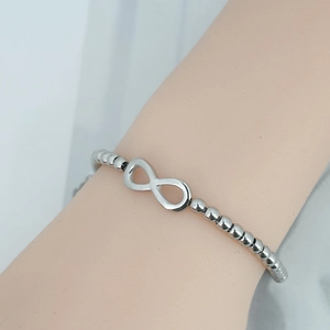 Polished silver beaded infinity bracelet on wrist featuring minimalist fashion design