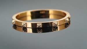 Close-up of rose gold stainless steel bangle with pyramid studs and Au750 engraving