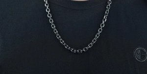 Detail of a minimalist stainless steel cable chain necklace worn over a black t-shirt