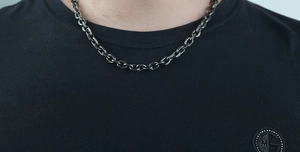 Detail of a dark grey stainless steel cuban chain necklace on a black shirt for men