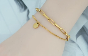 Gros plan d'un bracelet double couche doré à maillons trombones avec un pendentif rond